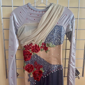 May include: A long-sleeved leotard featuring a silver metallic bodice with red and clear rhinestones. It includes a draped beige mesh overlay across the chest, dark gray sequined panels, nude mesh side cutouts, and red floral lace appliqués.
