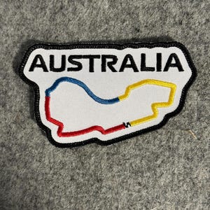 May include: White embroidered patch with the word "AUSTRALIA" in black capital letters. The patch features a colorful map outline in red, blue, and yellow, with a black border.