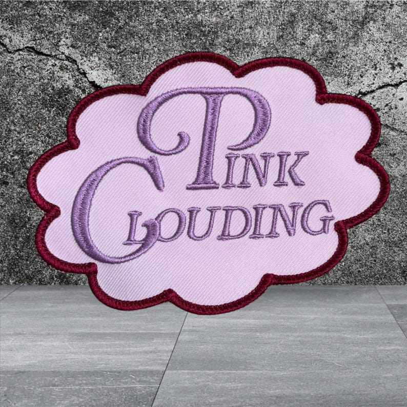 Puede incluir: Un parche bordado con forma de nube que presenta un fondo rosa claro con un borde granate oscuro. El texto "PINK CLOUDING" est&aacute; cosido en una fuente cursiva de color p&uacute;rpura en el centro del parche, creando un contraste visual distintivo.
