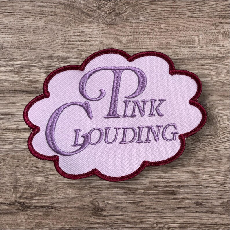 Puede incluir: Un parche bordado con forma de nube con fondo rosa claro y borde granate oscuro. El texto PINK CLOUDING est&aacute; bordado con hilo morado en el centro en una fuente serif decorativa con una P y una C grandes.