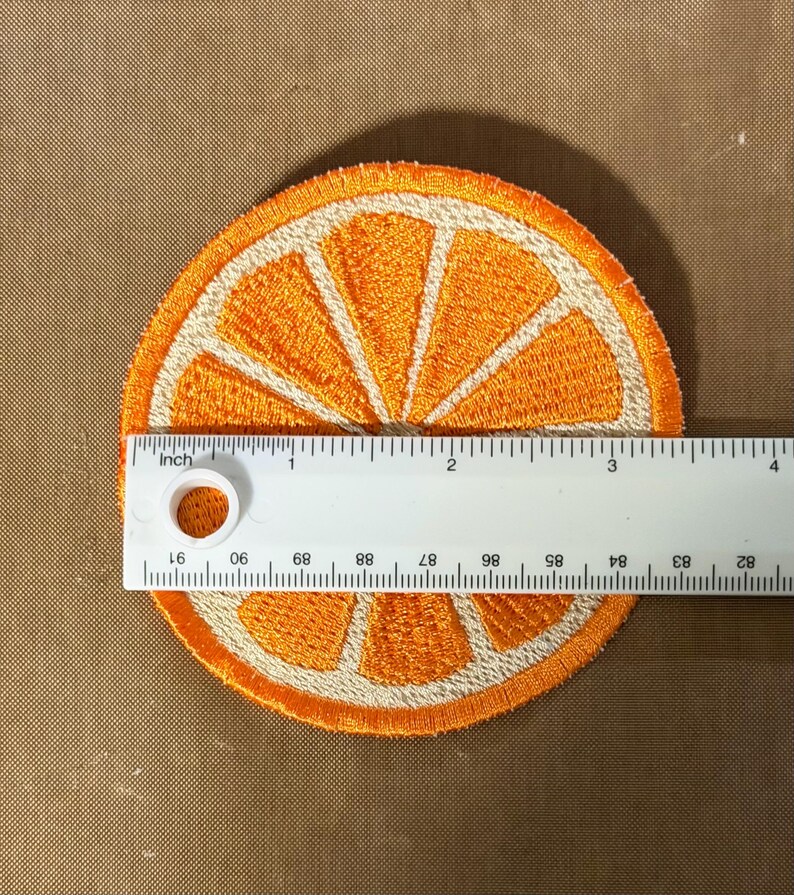 May include: Embroidered orange slice patch, approximately 3 inches in diameter. The patch features a bright orange color with white segments and a white border. The design is a detailed representation of a citrus fruit.