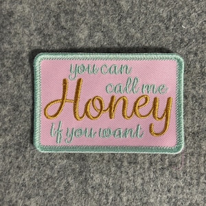 May include: Embroidered patch with a pink background and a light green border. The text "you can call me Honey if you want" is embroidered in gold and light green thread. The patch is rectangular.