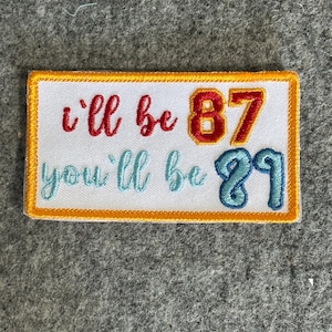 May include: White embroidered patch with orange, red, and blue lettering. The text reads "i'll be 87 you'll be 29".
