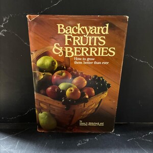 May include: A vintage book titled "Backyard Fruits & Berries" with a basket of colorful fruits on the cover. The book's cover features apples, grapes, and pears. The text reads "How to grow them better than ever."