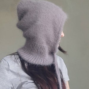 May include: A soft, grey hooded hat with a long, dangling tie. The hat is made of a fuzzy, knitted fabric.