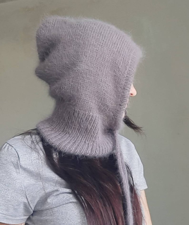 May include: A soft, grey hooded hat with a long, dangling tie. The hat is made of a fuzzy, knitted fabric.