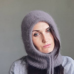 May include: A soft, grey hooded scarf with a long, dangling tie. The scarf is made of a fuzzy, knitted material.