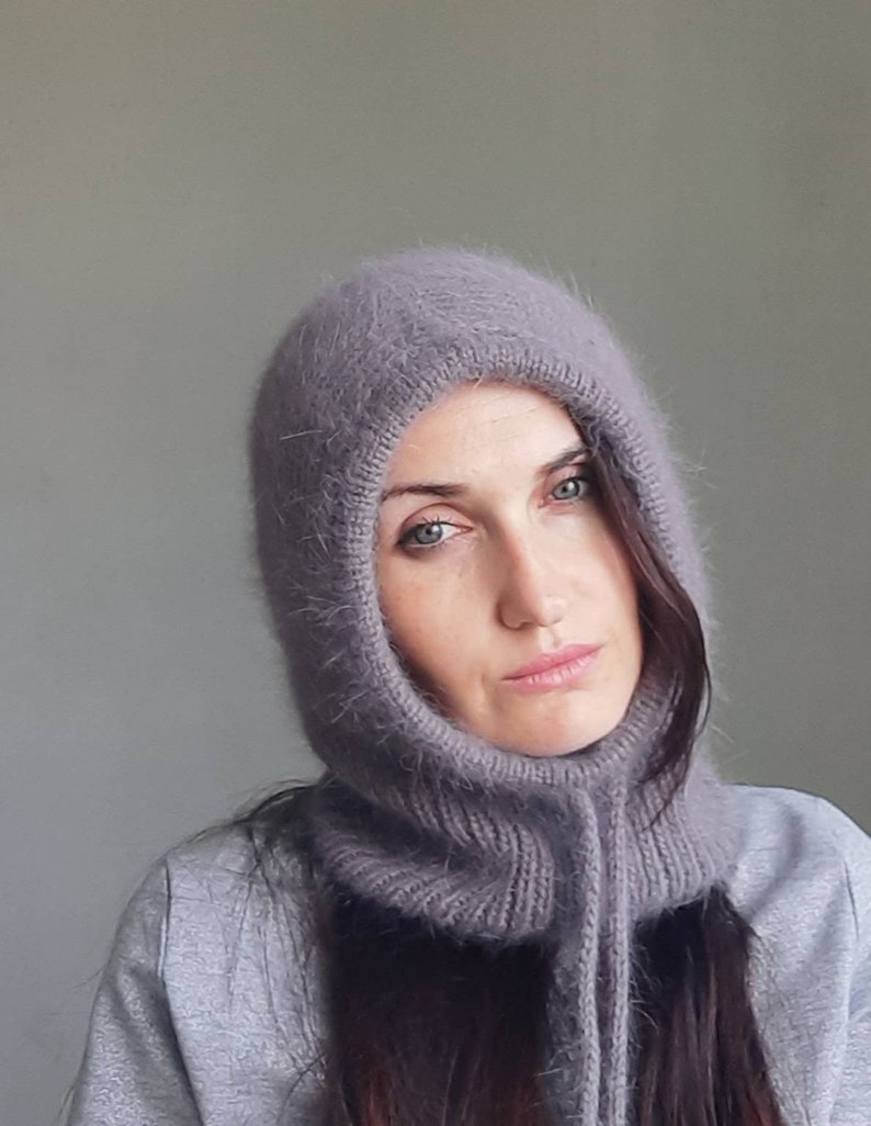 May include: A soft, grey hooded scarf with a long, dangling tie. The scarf is made of a fuzzy, knitted material.
