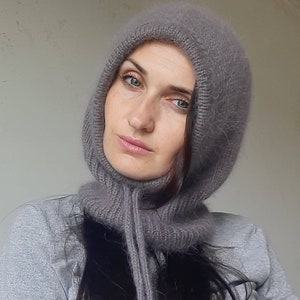 May include: A grey knitted hooded scarf with a long tassel. The scarf is made of a soft, fuzzy material.