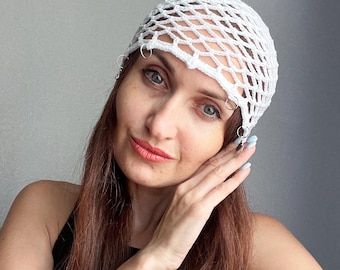 May include: A white crocheted hat with a net-like design and silver rings attached to the brim.