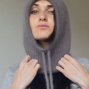 May include: A soft, grey hooded cowl with a long, fuzzy texture. The cowl has a drawstring tie at the neck.