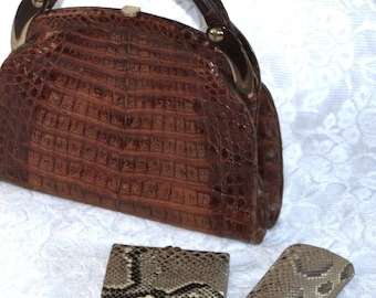 Peut inclure: Un sac à main en cuir de crocodile marron avec des ferrures dorées et une poignée supérieure. Le sac à main est accompagné de deux plus petites bourses assorties, une rectangulaire et une longue et étroite.