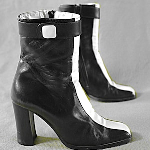 Peut inclure: Une paire de bottes à talons en cuir noir avec des accents blancs. Les bottes ont un talon épais et une fermeture éclair à l'intérieur de la cheville.