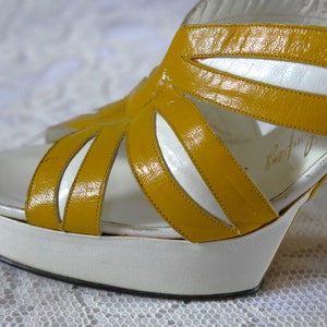 May include: Vintage platform sandals with a white sole and a mustard yellow upper. The open-toe design features cut-out details and a high heel. The sandals have a retro aesthetic, perfect for a vintage-inspired look.