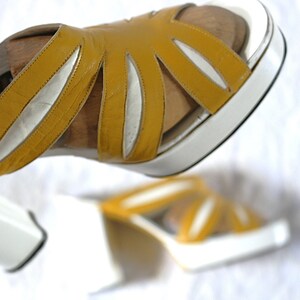May include: Mustard yellow leather sandals with a white platform sole. The sandals feature a unique cut-out design on the upper straps. The platform sole measures approximately 2 inches (5 cm) in height. The sandals are a stylish footwear choice.