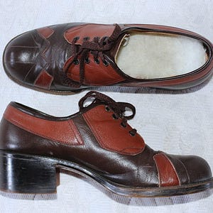 Könnte beinhalten: Zweifarbige braune und rotbraune Lederschuhe mit Schnürsenkeln. Die Schuhe haben einen Blockabsatz und eine runde Spitze. Der obere Schuh ist eine Draufsicht, der untere Schuh eine Seitenansicht. Die Schuhe scheinen Vintage zu sein.