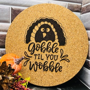 May include: A round cork trivet with a black and white turkey illustration and the text "Gobble til you wobble".