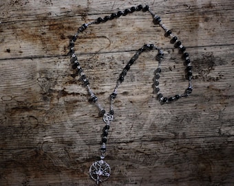 Peut inclure: Un collier de perles noires avec un pendentif pentagramme argenté. Le collier est sur une surface en bois.