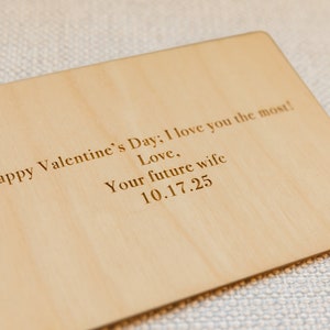 Puede incluir: Una tarjeta de madera con el texto "Happy Valentine's Day; I love you the most! Love, Your future wife 10.17.25" grabado en ella.
