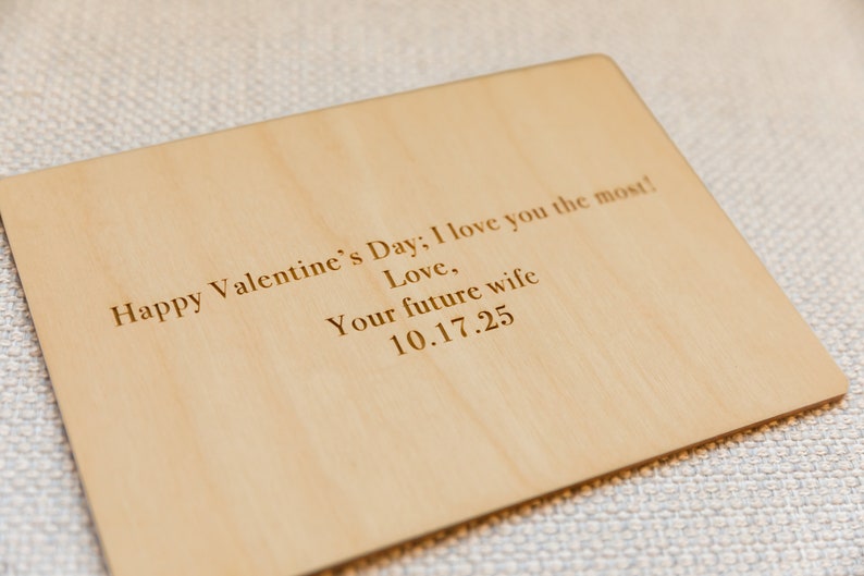 Puede incluir: Una tarjeta de madera con el texto "Happy Valentine's Day; I love you the most! Love, Your future wife 10.17.25" grabado en ella.