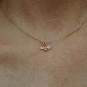 May include: A gold chain necklace with a small bee pendant adorned with tiny clear stones.