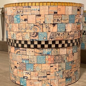 Op de afbeelding: Een ronde, decoratieve prullenbak met een mozaïekontwerp. De mozaïek is gemaakt van kleine, kleurrijke tegels in tinten blauw, roze en wit. De bovenkant van de prullenbak is afgewerkt met een gouden band.