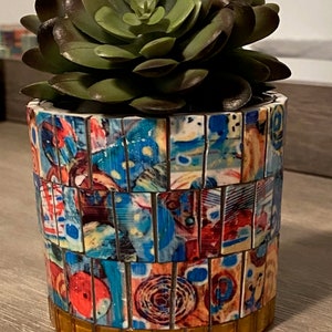 May include: A succulent plant in a colorful mosaic planter with a gold trim. The planter is made of small, square tiles in shades of blue, red, yellow, and white.