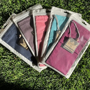 May include: Five drawstring bags in navy, purple, pink, teal, and burgundy, each sealed in a clear plastic pouch. Each bag has a matching drawstring and a tag that reads "GRACIE & ROO" with a crown logo. The bags are arranged on green grass.