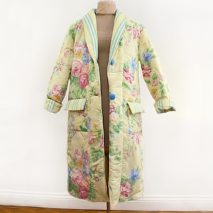 May include: A yellow quilted robe with a floral print and blue buttons. The robe has a white and green striped collar.