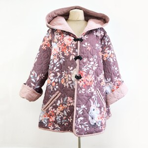 May include: A quilted jacket with a floral print and a hood. The jacket is pink with a brown quilted pattern and features a floral print with bunnies. The jacket has a toggle closure and is lined with a pink fabric.