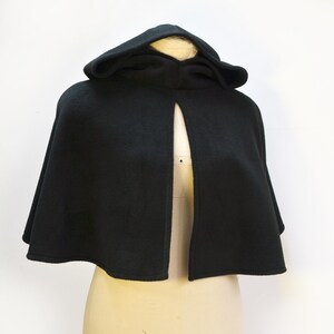 Mannequin wearing a black fleece capelet with a hood. The cape has a fixed opening and is approximately elbow length