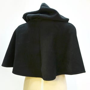 Black fleece cape shown from the back. It has a hood and it finishes just before the waist.