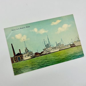 May include: A vintage postcard depicting a navy yard in Boston, Massachusetts. The postcard shows several ships docked at the yard, with a blue sky and white clouds in the background. The text "Navy Yard, Boston, Mass." is printed at the top of the postcard.