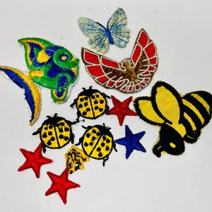 May include: A collection of embroidered patches featuring various designs. Includes a fish, butterfly, eagle, ladybugs, stars, and a bee. The patches are in vibrant colors such as yellow, blue, red, and black. These patches are suitable for clothing or craft projects.