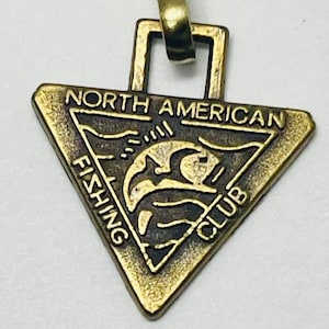 May include: A gold-toned triangular pendant with the words "North American Fishing Club" around the perimeter. A stylized fish design is in the center.