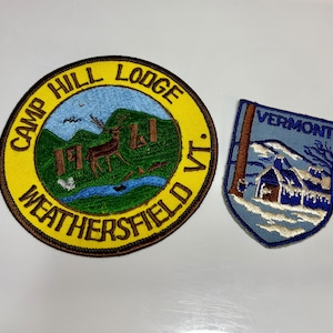May include: Two embroidered patches. One is round with "Camp Hill Lodge Weathersfield VT" around a deer and trees. The other is shield-shaped with "Vermont" above a winter scene with a cabin.