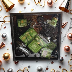May include: A black tray with a clear resin top filled with ice and various bottles of alcohol. The tray is decorated with gold glitter. The bottles include Jack Daniel's Tennessee Apple, a bottle of green liqueur, and a bottle of clear liquor.