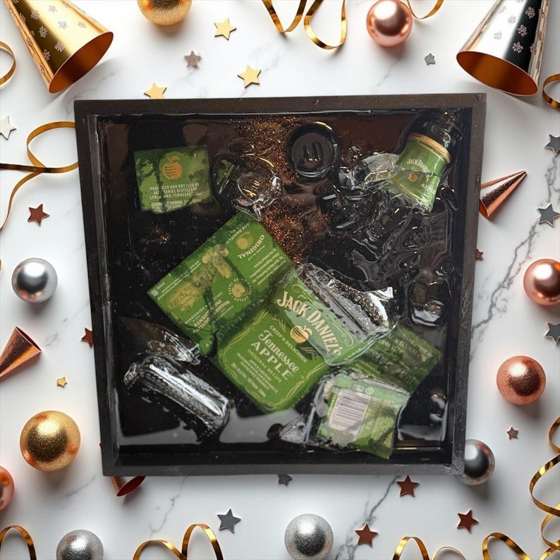 May include: A black tray with a clear resin top filled with ice and various bottles of alcohol. The tray is decorated with gold glitter. The bottles include Jack Daniel's Tennessee Apple, a bottle of green liqueur, and a bottle of clear liquor.