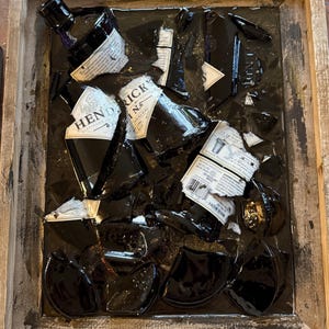 May include: A wooden frame holds a black resin art piece featuring broken glass bottles. The bottles are labeled "Hendrick's Gin" and "Tanqueray No. Ten Gin".