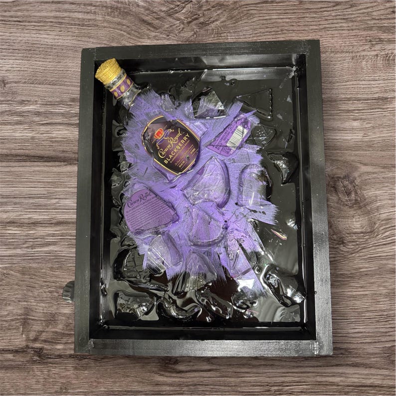 May include: A black framed resin art piece featuring a purple and black bottle of Crown Royal Blackberry liqueur in a black resin background with purple accents.