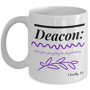 May include: White ceramic coffee mug with a black line and the word "Deacon" in black text. The text "holding the mystery of the faith with great boldness" is written in a purple font below the word "Deacon". A purple stylized branch is below the text. The text "1 timothy 3:8" is written in black at the bottom of the mug.