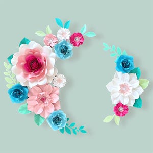 May include: A decorative arrangement of paper flowers in shades of pink, blue, and white. The flowers are arranged in a semi-circle shape and are accented with green paper leaves.