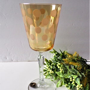 May include: A clear glass wine glass with a gold-colored stem and base. The glass has a polka dot pattern in a light brown color.