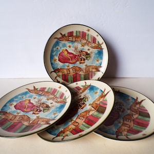 May include: Set of four decorative plates with a whimsical design. Each plate features a central image of an angel-like figure with the text "BLESS USA" on a banner. The plates have a cream-colored background with a green rim.
