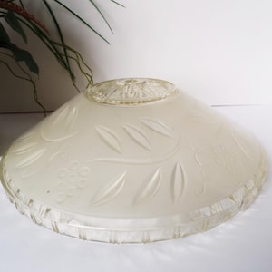 May include: A vintage, frosted glass lampshade with a decorative floral pattern. The shade has a wide, shallow bowl shape with etched leaves and grape clusters. The rim and top are clear glass.