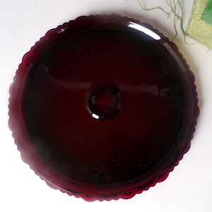 May include: A deep red glass cake plate with a scalloped edge and a fluted design. The plate is perfect for serving desserts or appetizers.