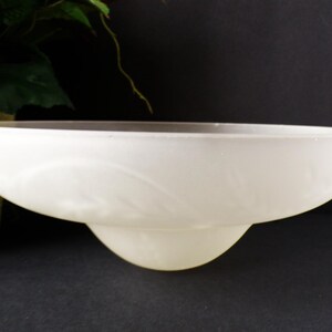 May include: A frosted glass bowl with a wide, shallow design and a rounded base. The bowl has a soft, white color and a subtle, etched pattern. The bowl is likely for decorative or serving purposes.