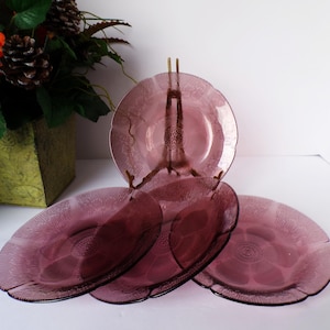 May include: Set of four vintage purple glass plates with a textured design. The plates have a scalloped edge and are displayed on a decorative brass plate stand. The plates are approximately 8 inches in diameter.