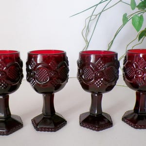 May include: Set of four ruby red glass wine goblets with a textured, diamond-shaped pattern. The goblets have a stemmed base and a round bowl.