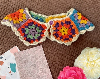 May include: A colourful crocheted collar with a scalloped edge and a button fastening. The collar is made in a granny square pattern with shades of orange, yellow, green, purple, and blue.